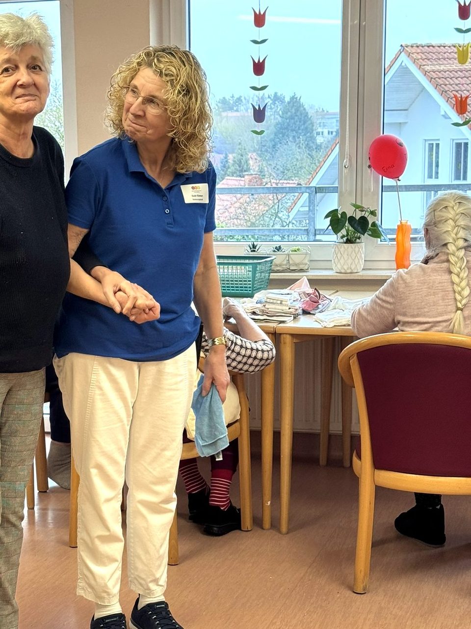 Pflegerin begleitet eine Bewohnerin durch den Wohnbereich der Wohngruppe